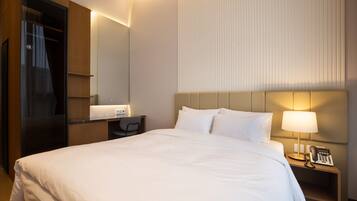 A hotel room with a large bed, a desk with a chair, a bedside lamp, and a telephone.