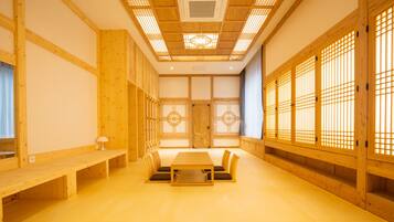 Una habitación japonesa tradicional con suelo de tatami, una mesa de madera baja con cojines y puertas correderas con diseños de celosía.