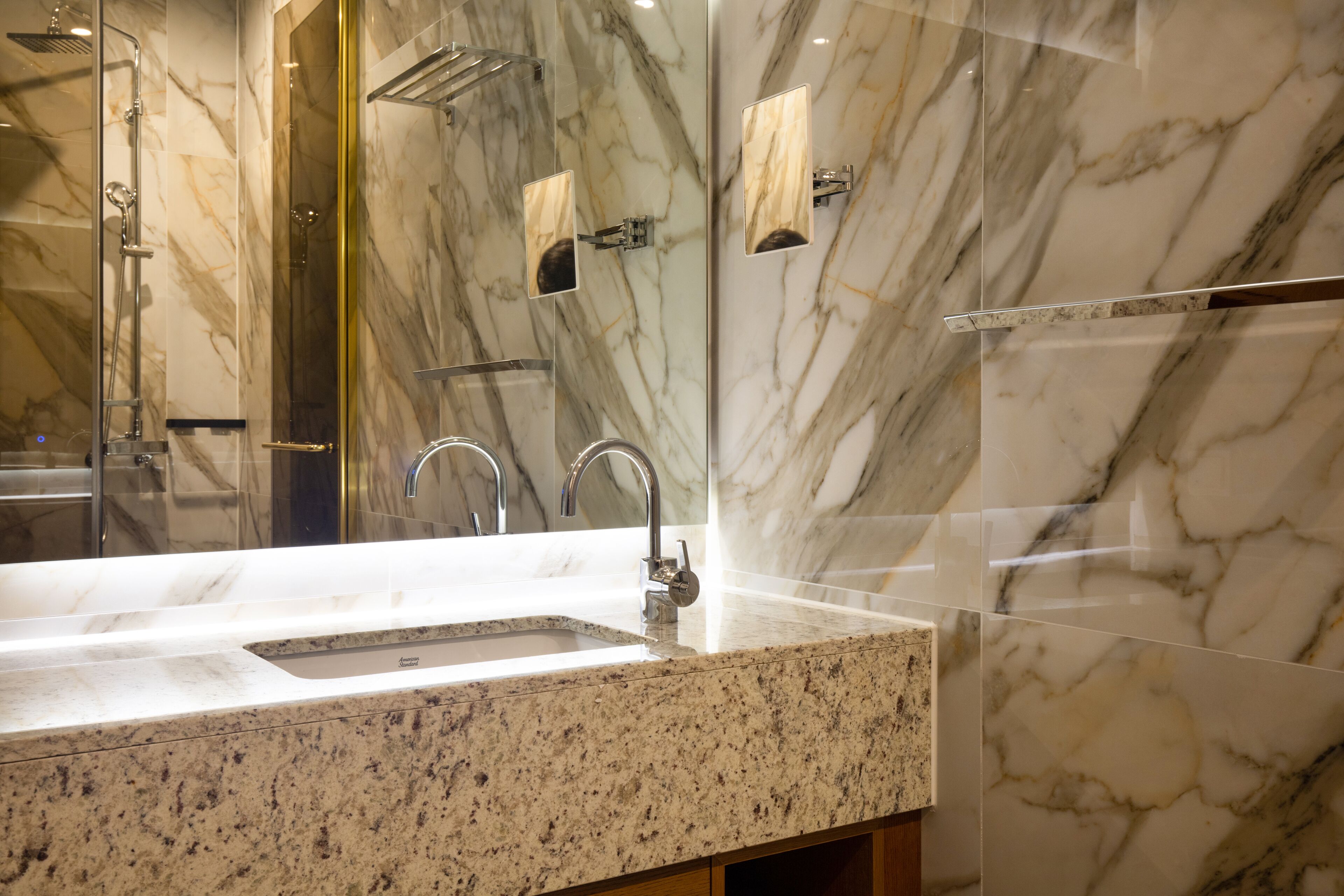 Une salle de bain avec un lavabo en marbre, une douche et un miroir encadré de verre.