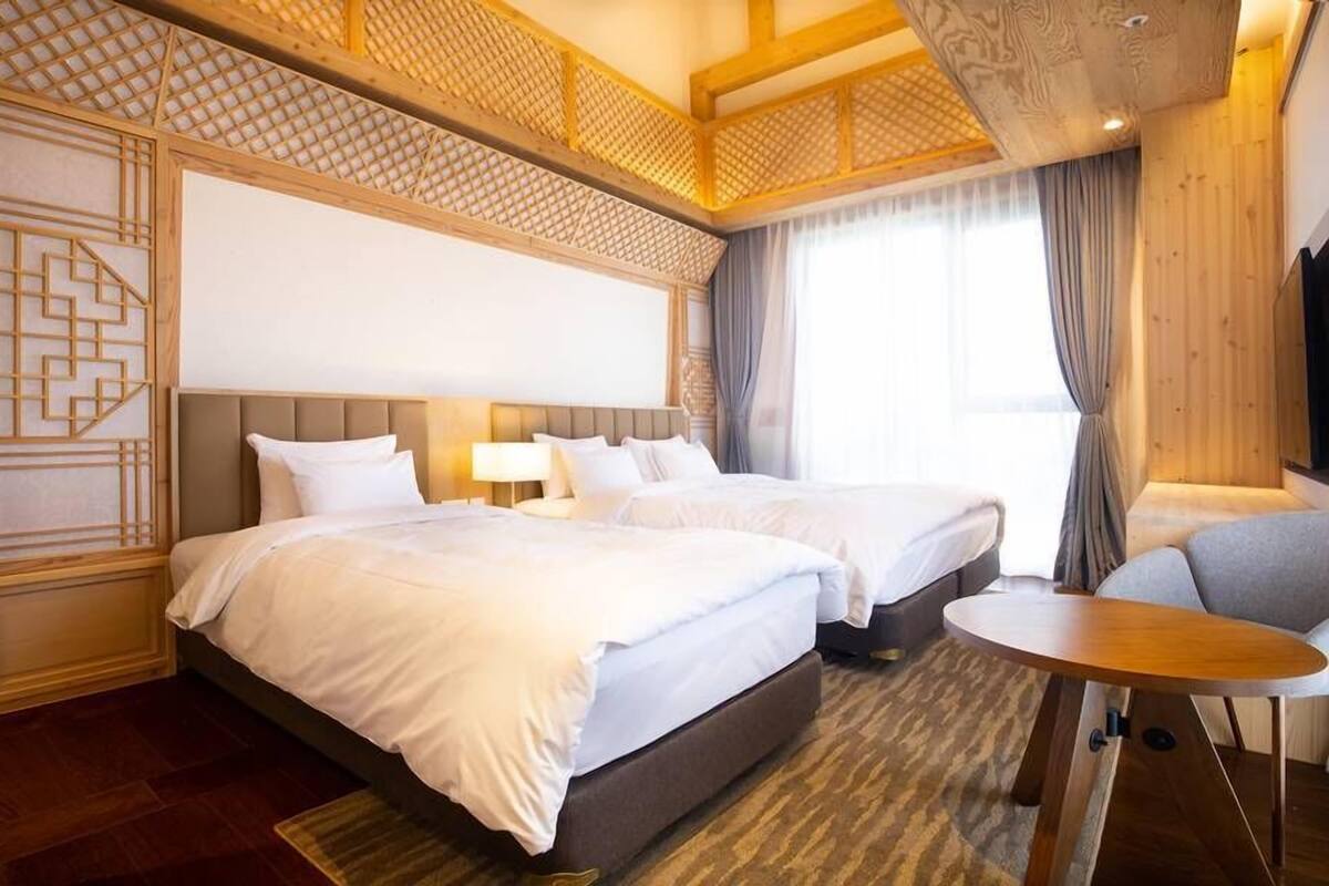 Habitación de hotel con dos camas, una mesita y vistas al exterior.