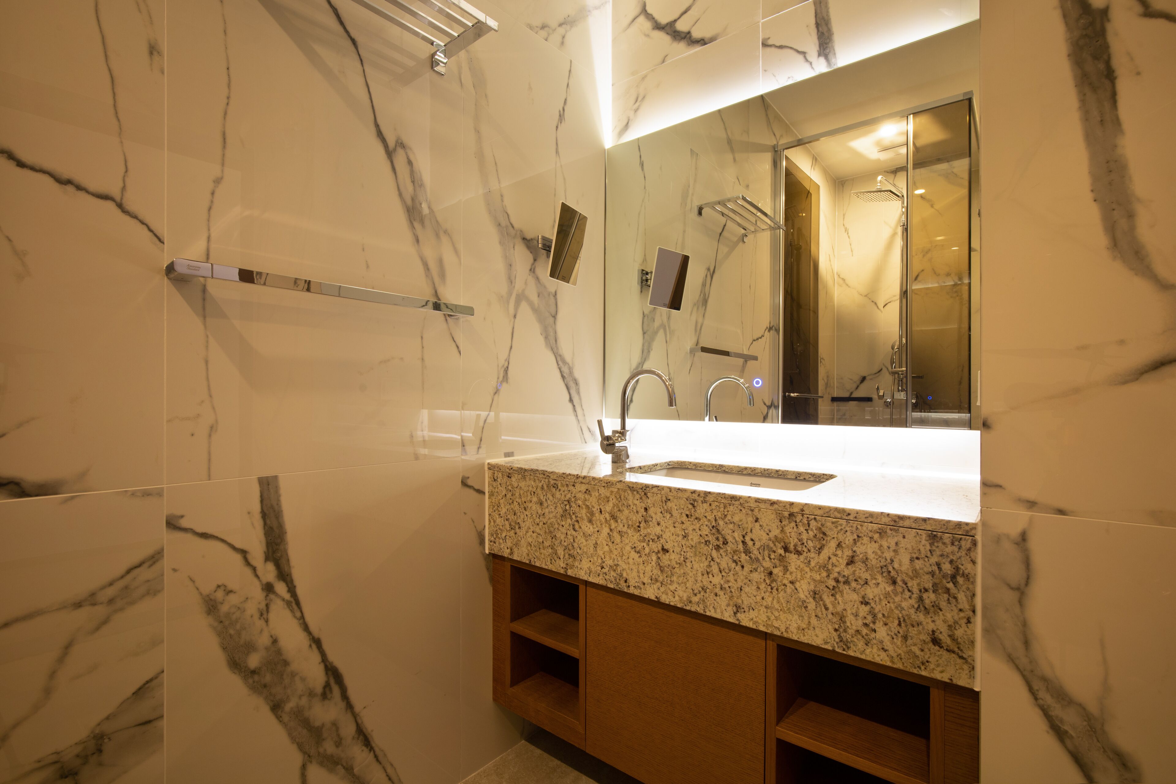 A bathroom with a marble wall, a sink with a granite countertop, and a mirror.