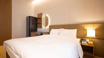 A hotel room with a large bed, a bedside table with a lamp, a phone, and a mirror with lights.