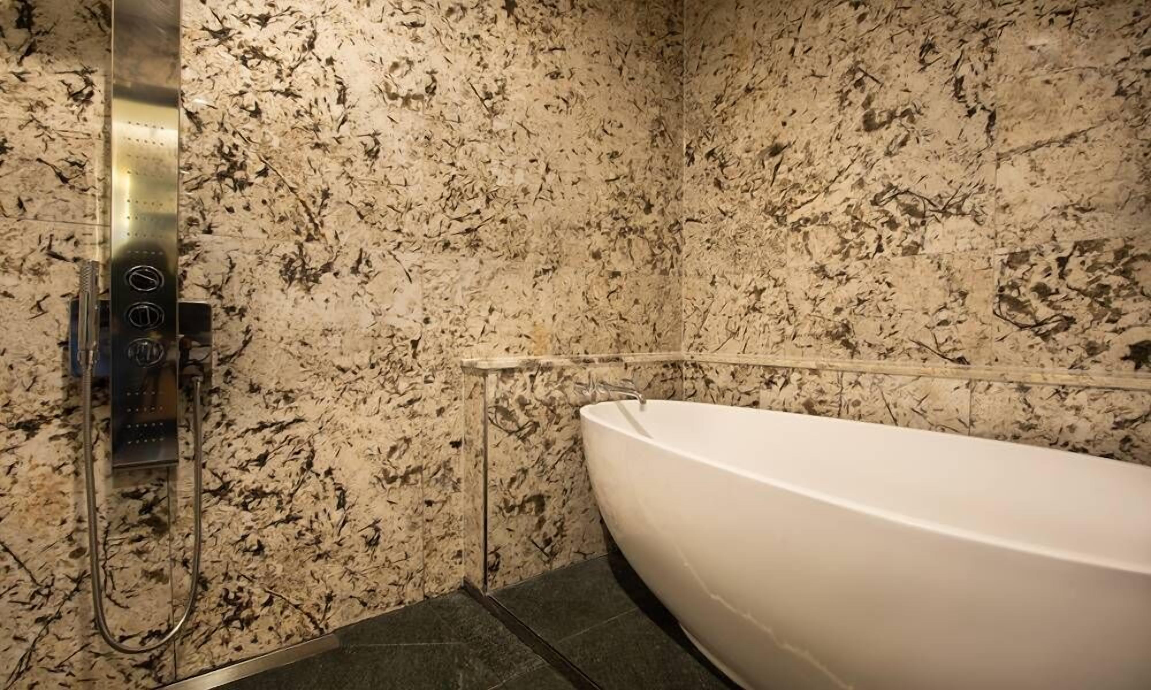 A bathroom with a white bathtub, a shower with a control panel, and a speckled marble wall.