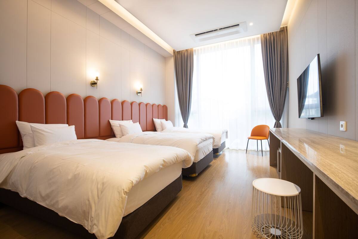 Habitación de hotel con dos camas, televisión, zona de bar y vistas al exterior.