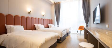 A hotel room with two beds, a TV, a bar area, and a view of the outdoors.