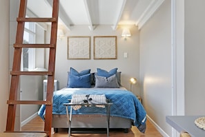 A bedroom with a bed, a ladder, a bedside table, and wall-mounted lights.