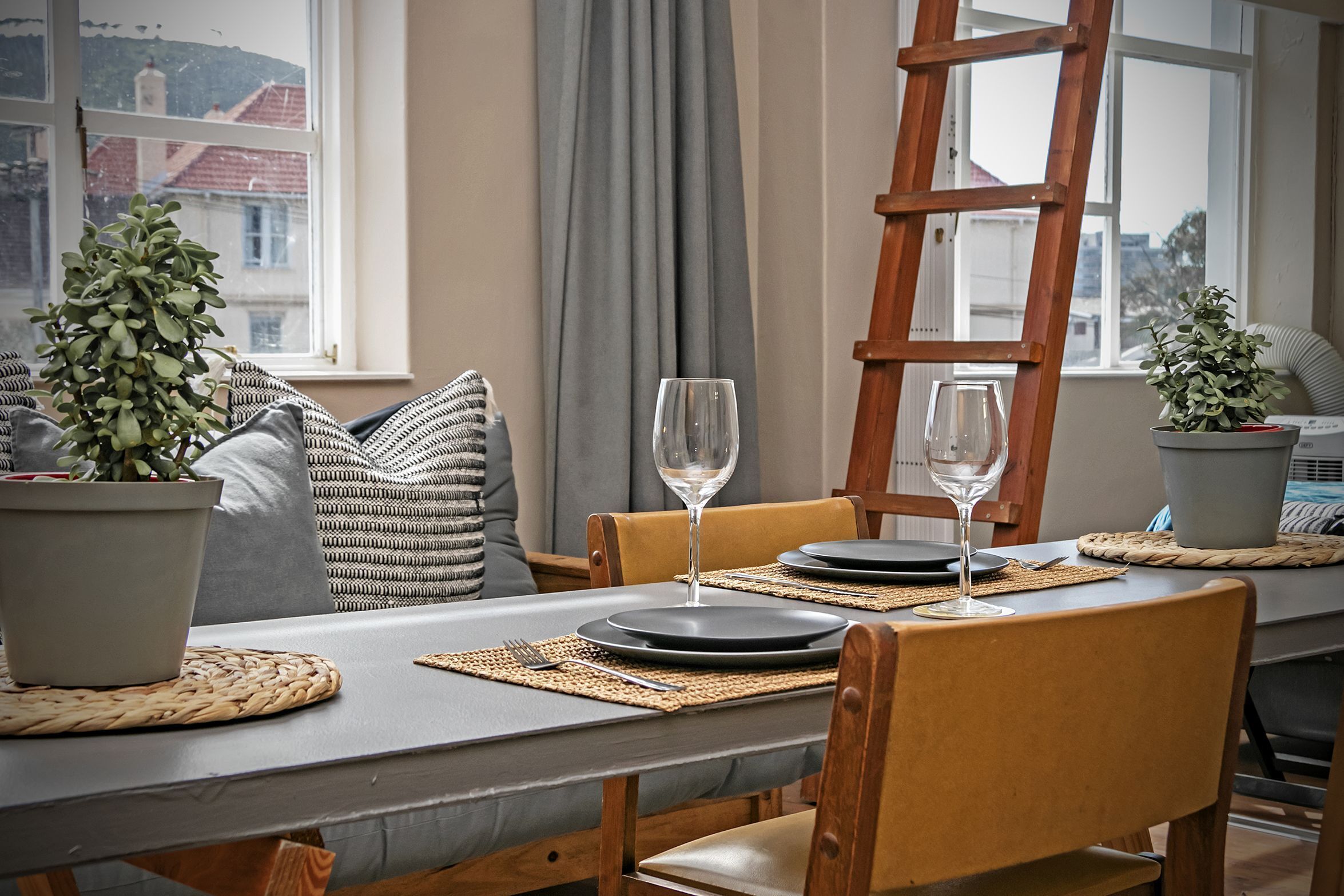 A dining area with a table set for two, featuring a wooden chair, a woven placemat, and a potted plant.