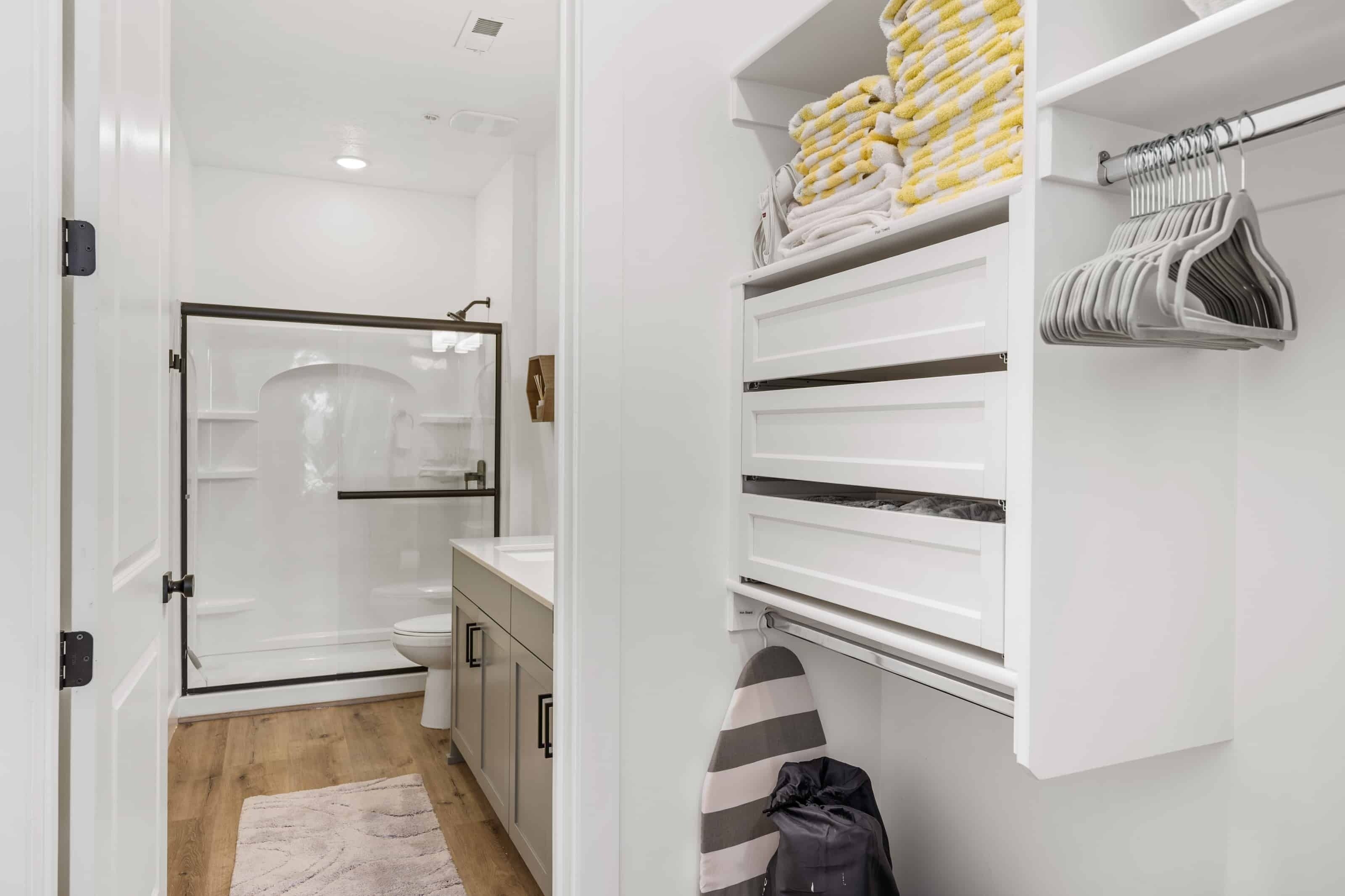 A modern bathroom with a glass shower enclosure, white cabinetry, and a towel rack with folded towels.