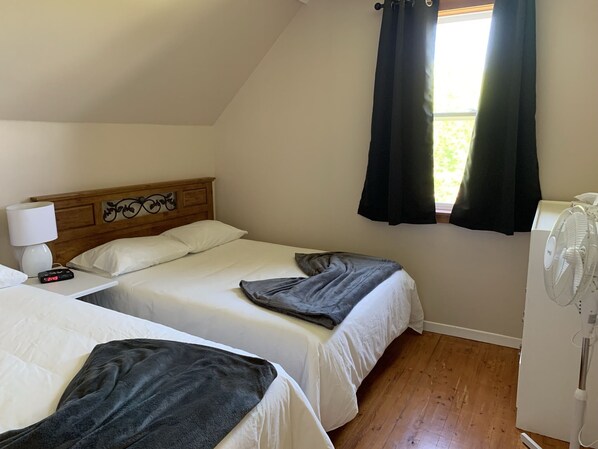 A room with two beds, a nightstand with a lamp, a clock, and a window with curtains.