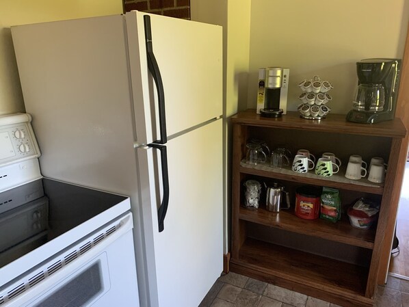 A kitchen with a white refrigerator, a coffee maker, and a shelf with mugs and coffee cups.