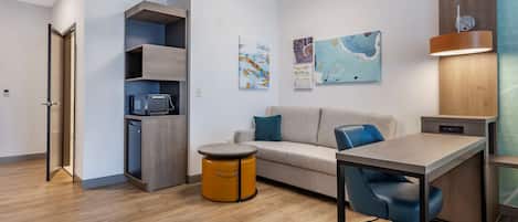 A modern, compact living space with a kitchenette, a sofa, a dining table, and a small round table.