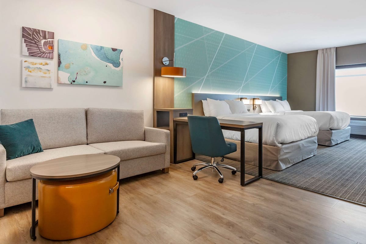 A modern hotel room with a sofa, a desk, a chair, a bed, and artwork on the wall.