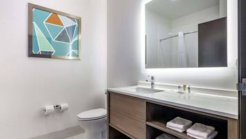 A modern bathroom with a toilet, sink, and mirror. There is a framed abstract artwork on the wall and a towel rack with towels.