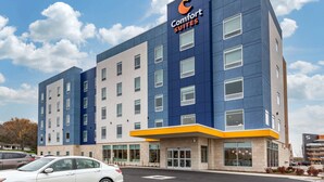 A Comfort Suites hotel with a modern design, featuring a prominent blue and yellow color scheme, large windows, and a parking lot with several cars. - Comfort Suites Cottage Grove – Madison (Cottage Grove)