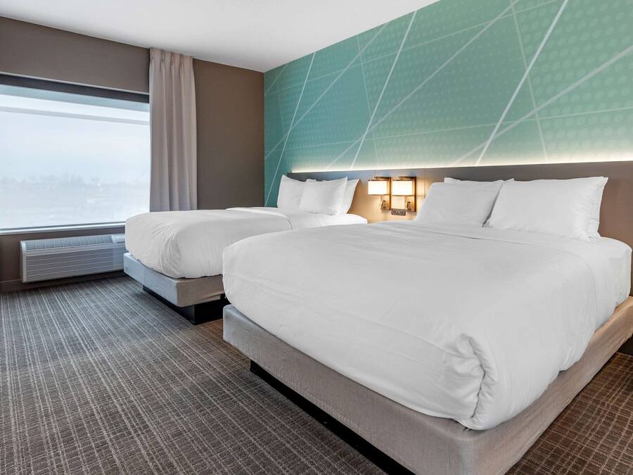 Habitación de hotel con dos camas, un ventanal con cortinas, un aire acondicionado de pared y una alfombra estampada.