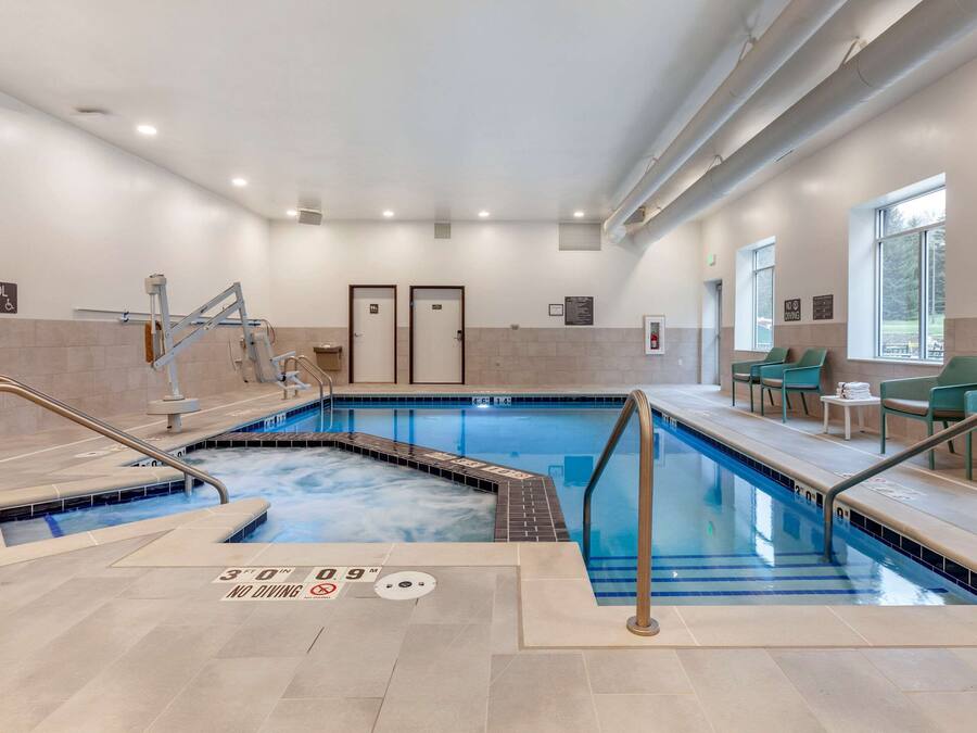 An indoor swimming pool with clear signage, a lifeguard stand, and a seating area with chairs.