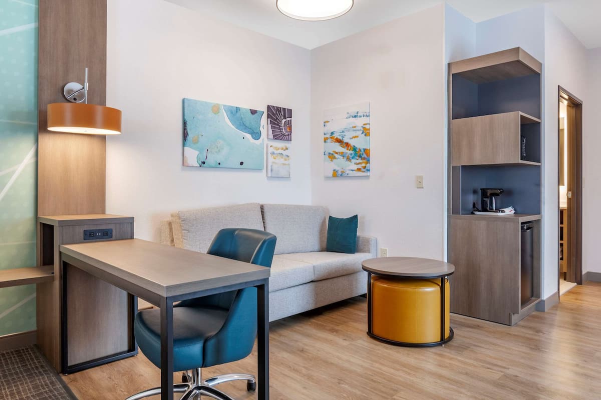 A modern living room with a sofa, a dining table, and a coffee table. There is a wall-mounted light fixture and artwork on the wall.