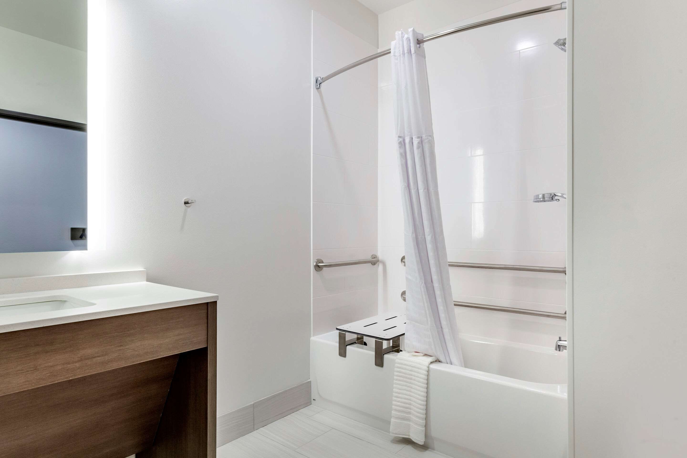 A modern bathroom with a white bathtub, a shower with a curtain, and a vanity with a mirror.