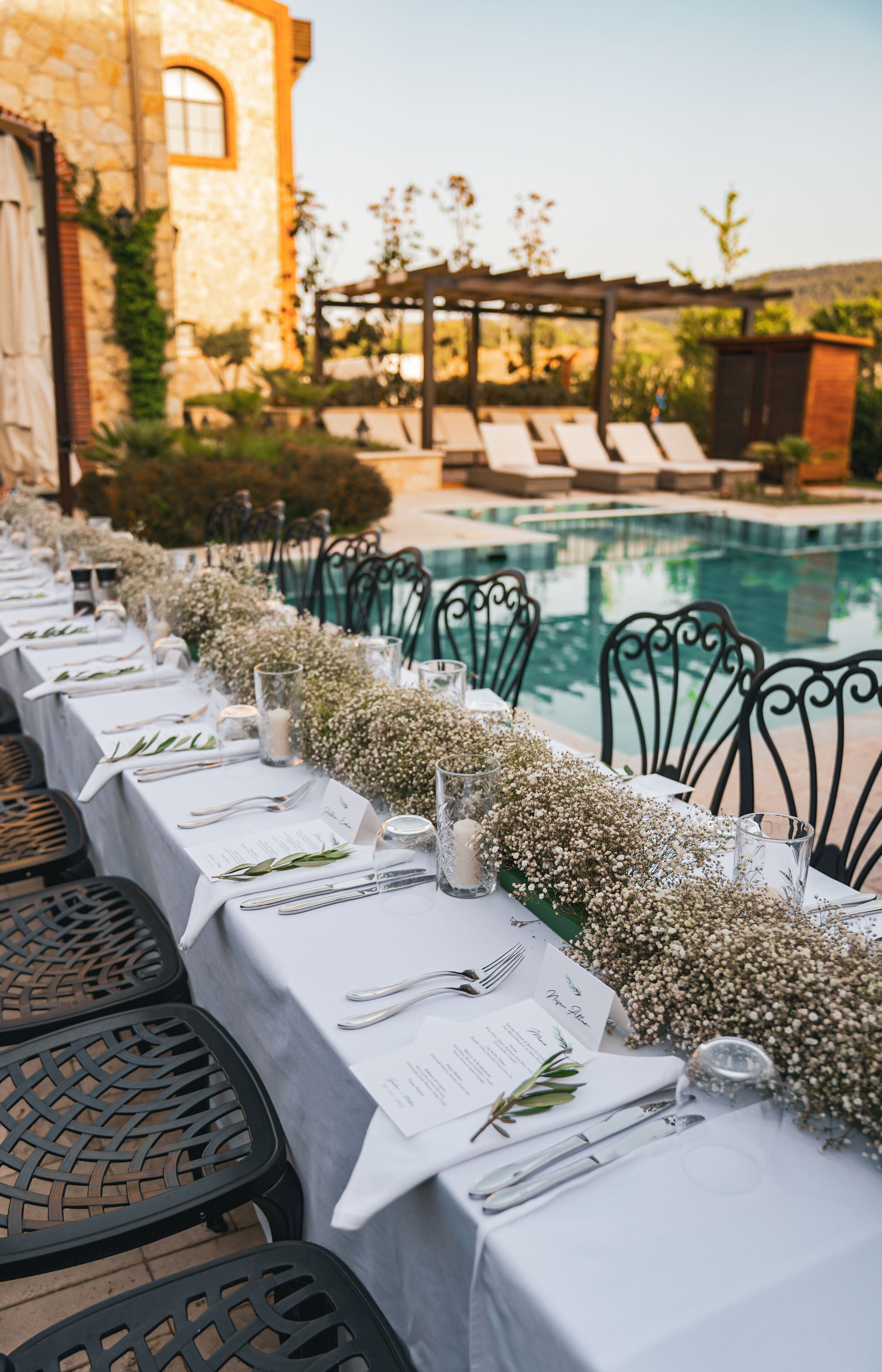 A poolside dining area with tables set for a meal, overlooking a pool and a garden.