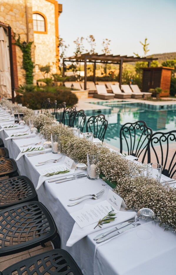 A poolside dining area with tables set for a meal, overlooking a pool and a garden.