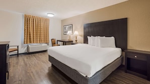 A hotel room with a large bed, a desk, a chair, a lamp, and a heater. - Econo Lodge Vidalia (Vidalia)