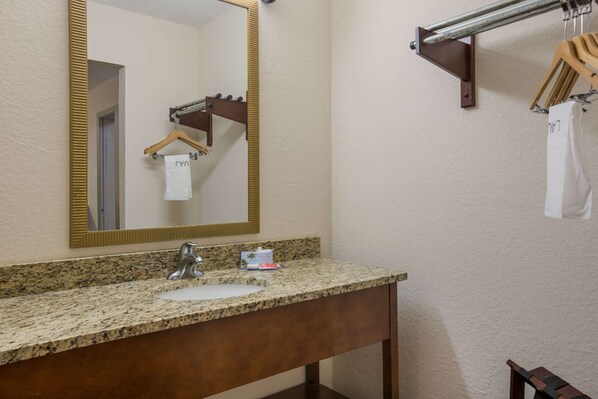 A bathroom with a granite countertop sink, a mirror with a gold frame, and a towel rack with hangers.