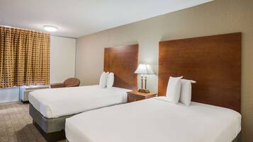 Quarto de hotel com duas camas, uma escrivaninha, uma cadeira, um abajur e uma janela com cortinas.