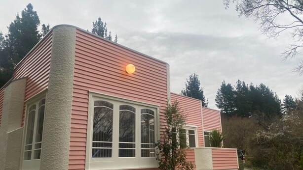 Una casa con facciata rosa, rivestimenti bianchi e un piccolo giardino antistante.
