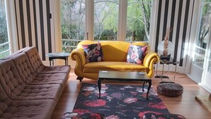 Un soggiorno con un divano marrone, un divano giallo con cuscini a motivi floreali, un tavolino da caffè e un tappeto decorato.