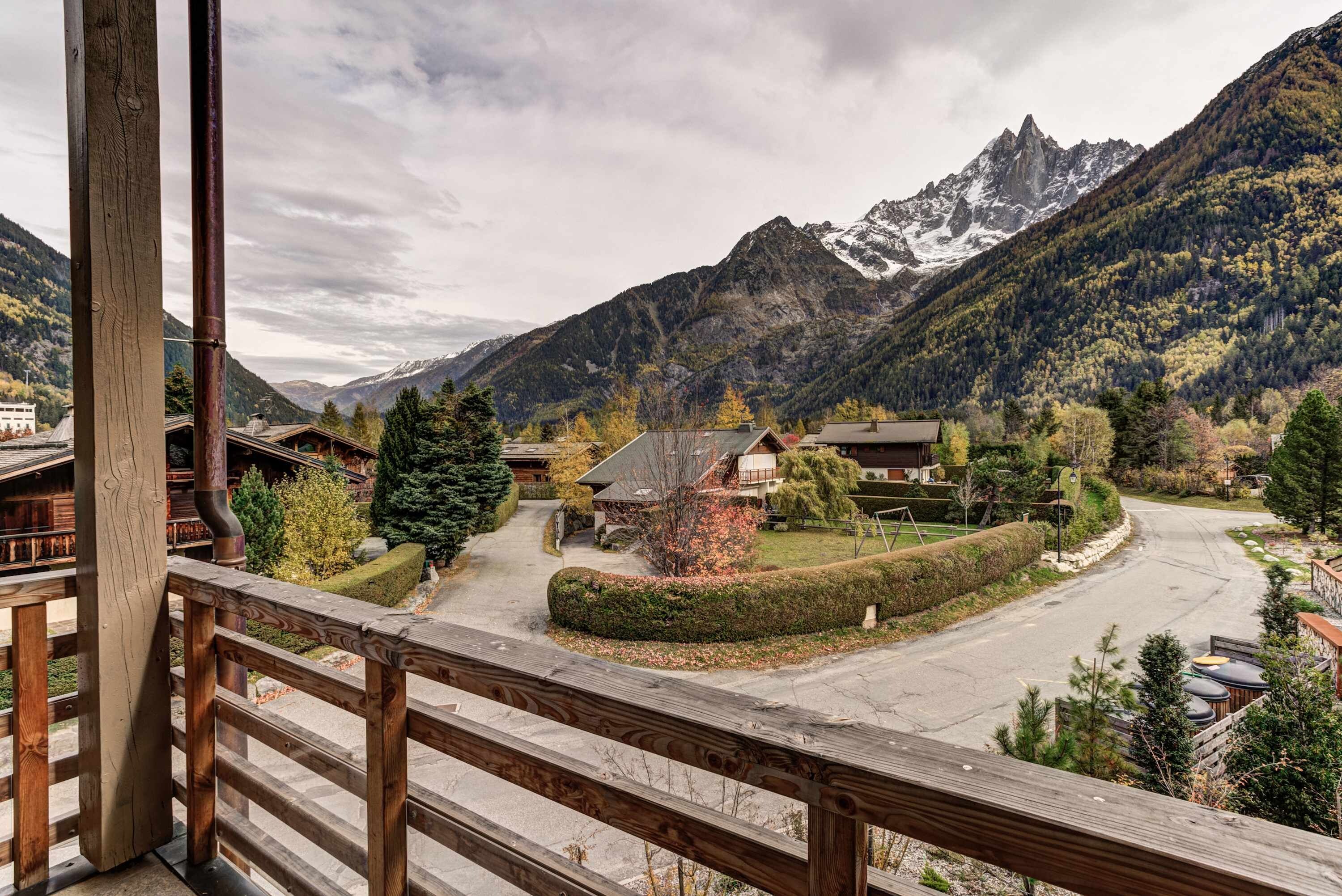 Un village de montagne aux maisons traditionnelles en bois, avec une route dégagée et une vue sur des montagnes enneigées.