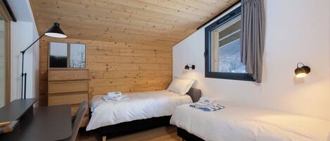 A compact bedroom with two beds, a desk, and a window with curtains.