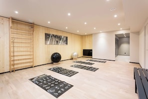 Een moderne spa ruimte met houten lambrisering, een groot schilderij, yogamatten en een houten bank.