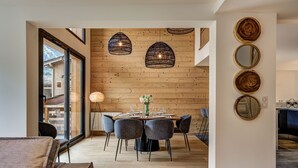 A modern dining area with a wooden wall, a round table set for six, and a large window. - La Cordee 221 Penthouse -  sleeps 8 guests with pool, sauna, gym, parking (Chamonix-Mont-Blanc)
