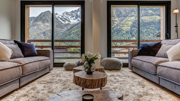 A modern living room with a large window offering a mountain view, a round wooden coffee table, and two sofas with cushions. - La Cordee 221 Penthouse -  sleeps 8 guests with pool, sauna, gym, parking (Chamonix-Mont-Blanc)