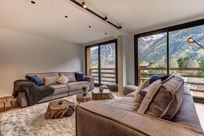 Een moderne woonkamer met een bank, salontafel en uitzicht op bergen door grote ramen.
