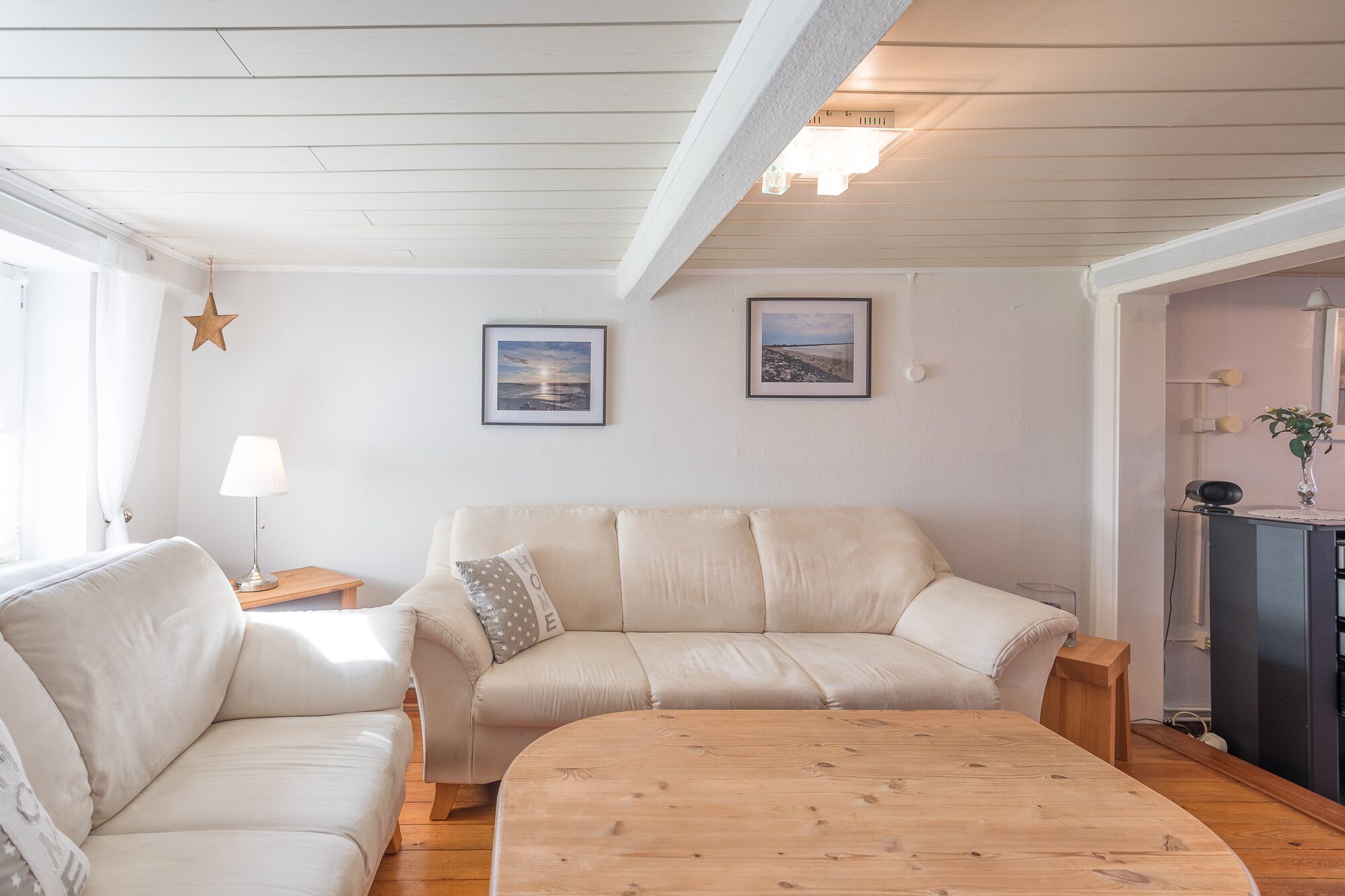 Uma sala de estar com um sofá, uma mesa de centro de madeira e duas fotos emolduradas na parede.
