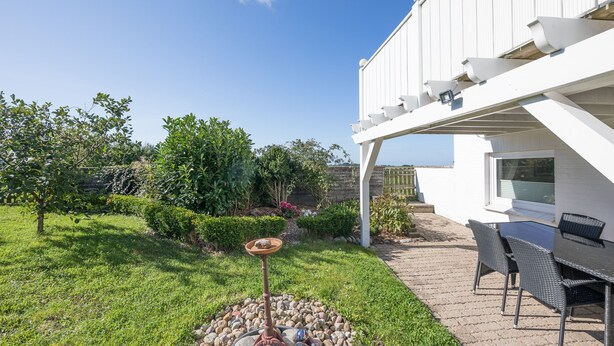 Eine Terrassenfläche mit Tisch und Stühlen, einem Vogelbad und einem Garten mit verschiedenen Pflanzen und einem Baum.