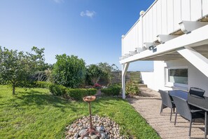 A patio area with a table and chairs, a birdbath, and a garden with various plants and a tree. - Sputnik Vacation Home in Nordstrand for up to 5 people (Nordstrand)