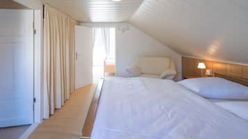 A bedroom with a large bed, a chair, a bedside table with a lamp, and a door leading to another room.