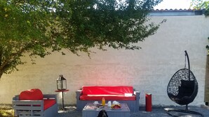 An outdoor seating area with a red sofa, a hanging chair, and a dog sitting on the ground. - Beautiful house in the country (LE FRAYSSE)