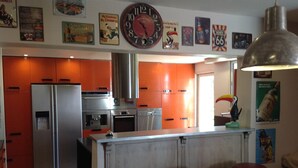 A kitchen with stainless steel appliances, a central island with stools, and a large wall clock. - Beautiful house in the country (LE FRAYSSE)