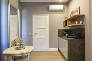 A compact kitchen with a microwave, coffee maker, and a shelf with mugs. - Vespucci Boutique (Stresa)
