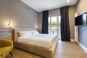 A modern hotel room with a large bed, a yellow armchair, a TV, and a balcony with curtains. - Vespucci Boutique (Stresa)