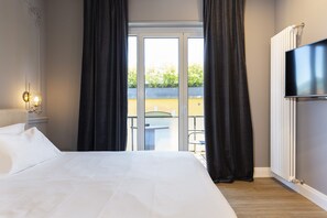 A hotel room with a large bed, a TV, a sliding glass door to an outdoor area, and a radiator. - Vespucci Boutique (Stresa)