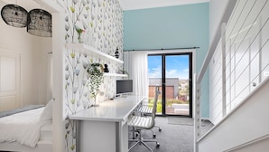 Een moderne slaapkamer met een bed, een bureau met een computer, een stoel en uitzicht op het buitenlands gebied door een glazen deur.
