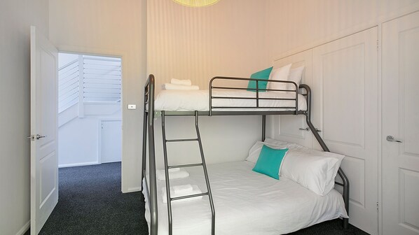 A bunk bed room with a ladder, white bedding, and a teal pillow.
