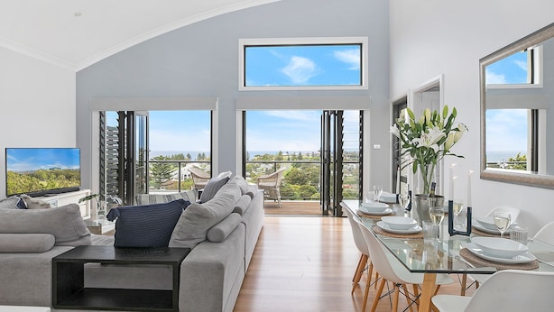 Een ruime woonkamer met balkon, een eethoek met glazen tafel en een grote televisie aan de linkerkant.