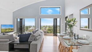A spacious living room with a balcony, a dining area with a glass table, and a large TV on the left.