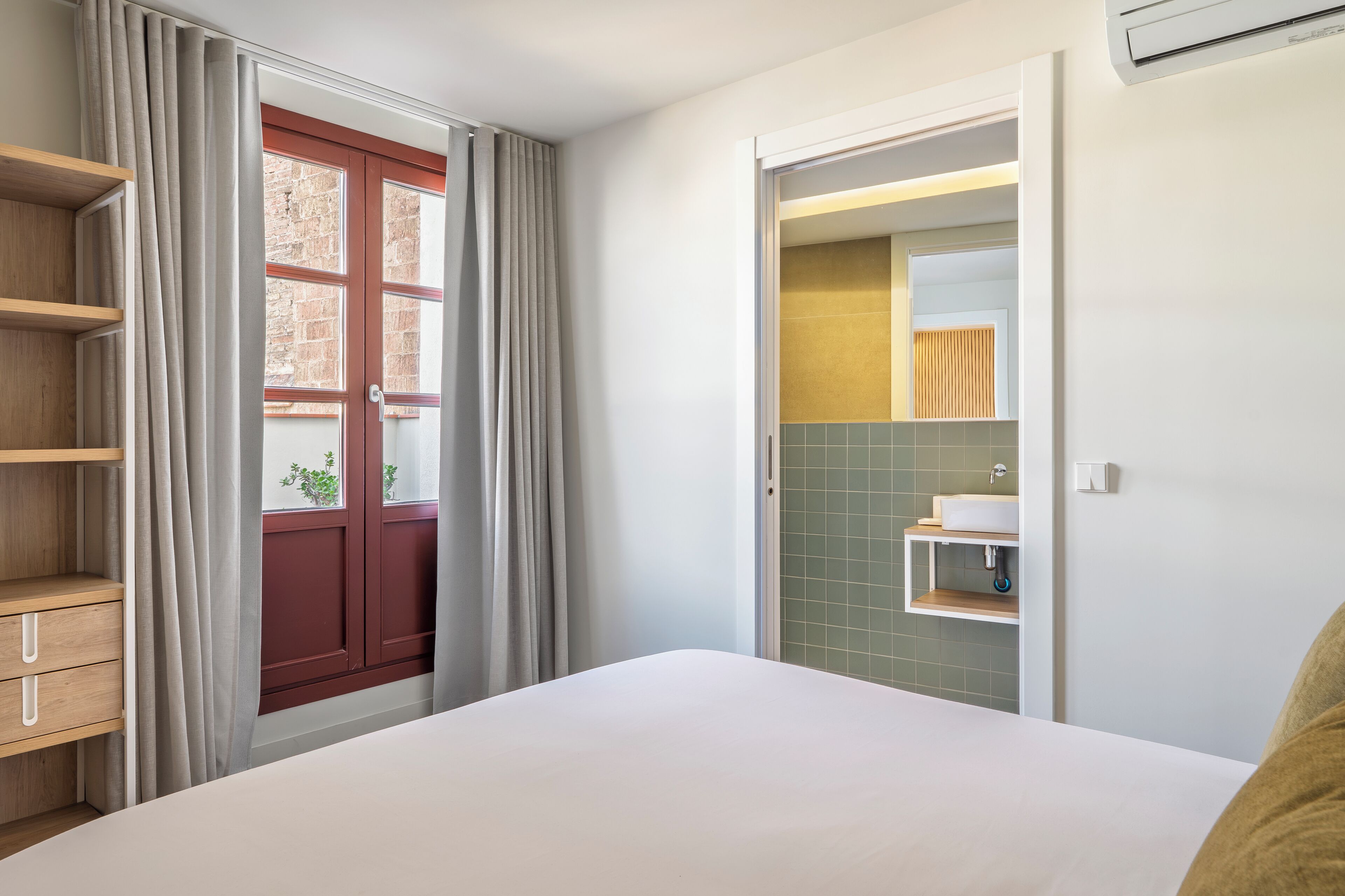 Une chambre à coucher comprenant un lit, une armoire, une salle de bain avec un lavabo et un miroir, et une fenêtre avec des rideaux.