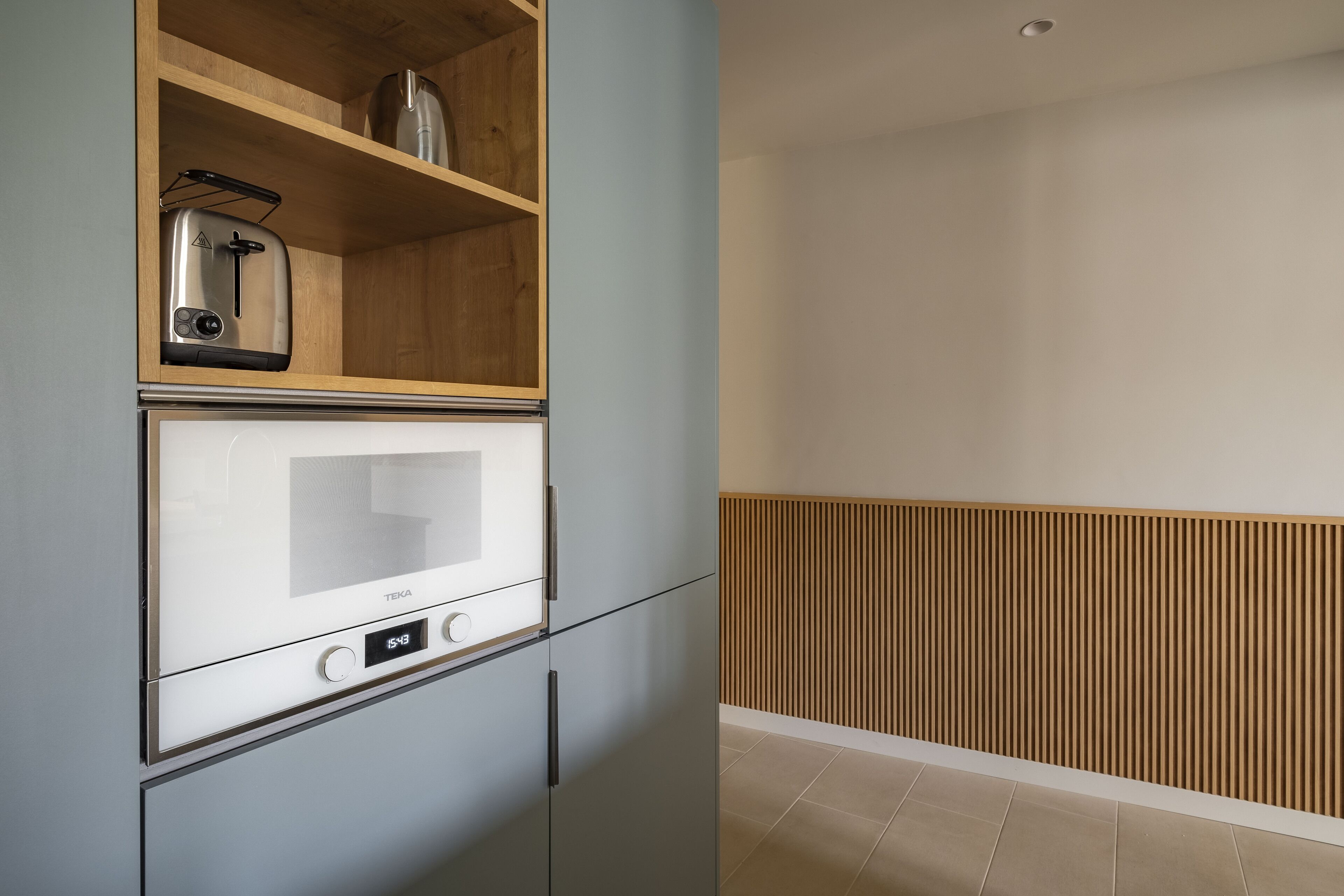 Una cocina moderna con microondas y tostadora integrados, estantes de madera y un diseño elegante.